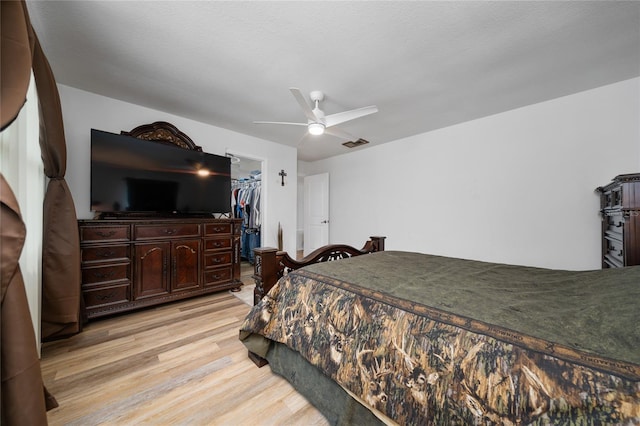 bedroom featuring a closet, a walk in closet, light hardwood / wood-style floors, and ceiling fan