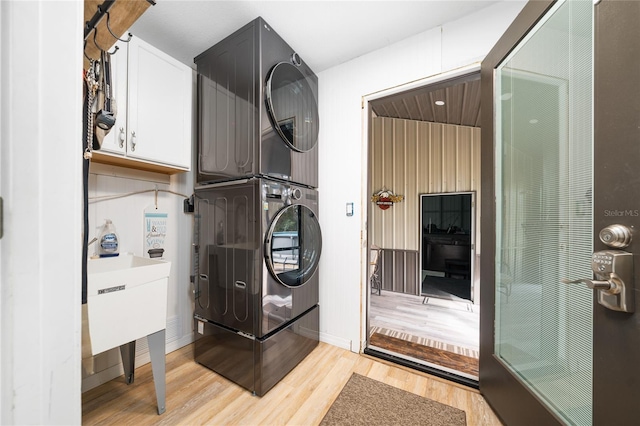 clothes washing area with stacked washing maching and dryer, cabinets, light hardwood / wood-style flooring, and sink