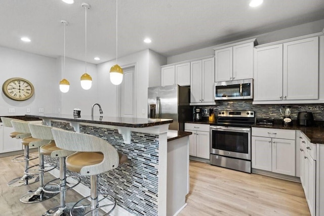 kitchen featuring a breakfast bar, white cabinetry, tasteful backsplash, decorative light fixtures, and appliances with stainless steel finishes