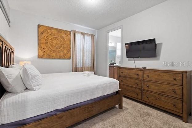 bedroom featuring light colored carpet, a textured ceiling, and ensuite bathroom