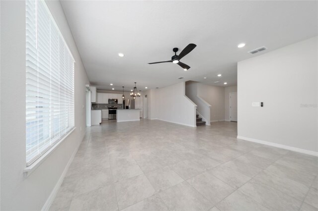 unfurnished living room featuring ceiling fan with notable chandelier