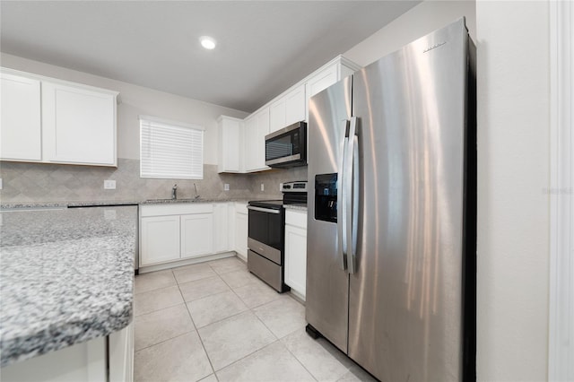 kitchen featuring light tile patterned floors, appliances with stainless steel finishes, backsplash, light stone countertops, and white cabinets