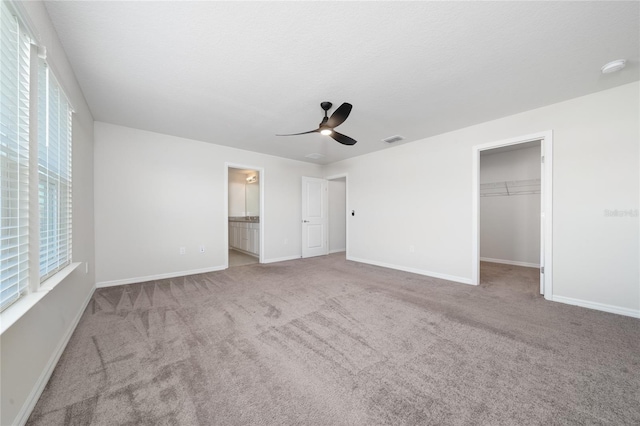 unfurnished bedroom featuring a spacious closet, ensuite bathroom, ceiling fan, carpet, and a closet