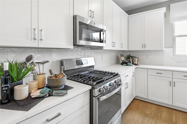 kitchen with light stone countertops, appliances with stainless steel finishes, white cabinets, light wood-type flooring, and backsplash