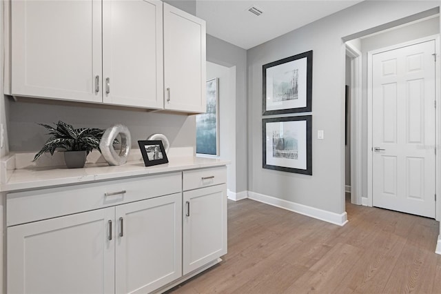 kitchen featuring light wood-type flooring, white cabinetry, and light stone counters