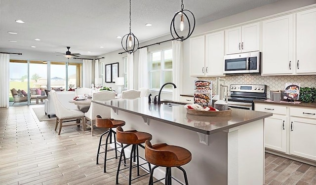 kitchen with decorative light fixtures, decorative backsplash, sink, appliances with stainless steel finishes, and an island with sink