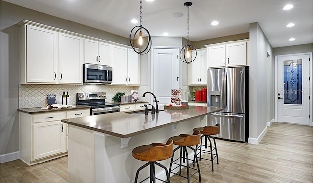 kitchen with white cabinets, stainless steel appliances, an island with sink, sink, and hanging light fixtures