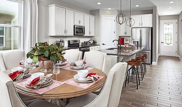 kitchen with appliances with stainless steel finishes, white cabinetry, tasteful backsplash, an island with sink, and hanging light fixtures