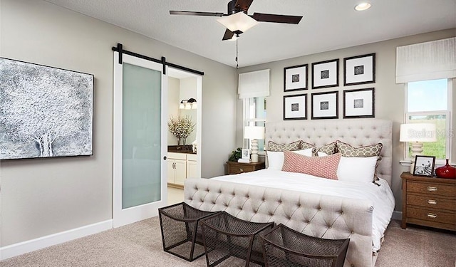 bedroom featuring ceiling fan, light colored carpet, ensuite bathroom, and a barn door