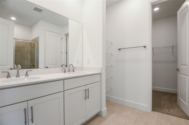 9093 Players Dr, Weeki Wachee, FL 34613 - bathroom featuring a stall shower, double vanity, a spacious closet, wood finished floors, and recessed lighting