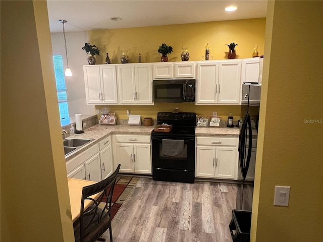 kitchen with decorative light fixtures, white cabinetry, sink, black appliances, and light wood-type flooring