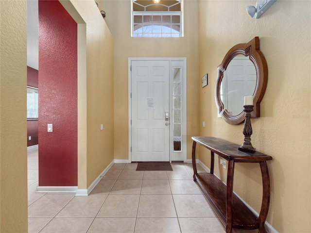 foyer entrance with light tile patterned floors, a high ceiling, baseboards, and a textured wall