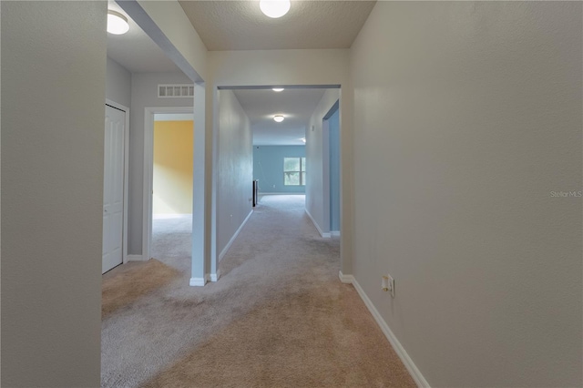 corridor with light carpet and a textured ceiling