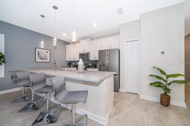 kitchen featuring a kitchen bar, appliances with stainless steel finishes, hanging light fixtures, white cabinets, and sink