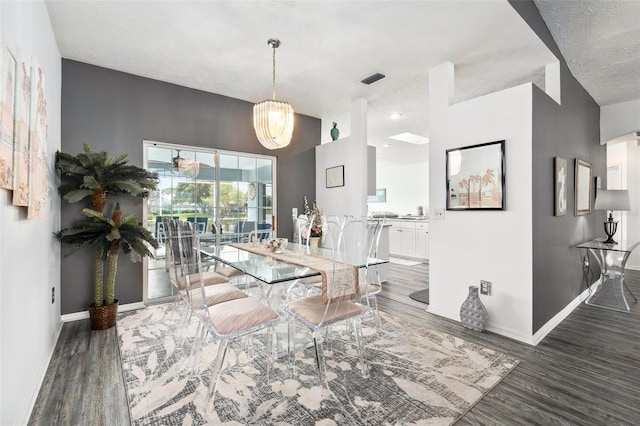 dining space featuring dark wood-type flooring, a textured ceiling, and a notable chandelier