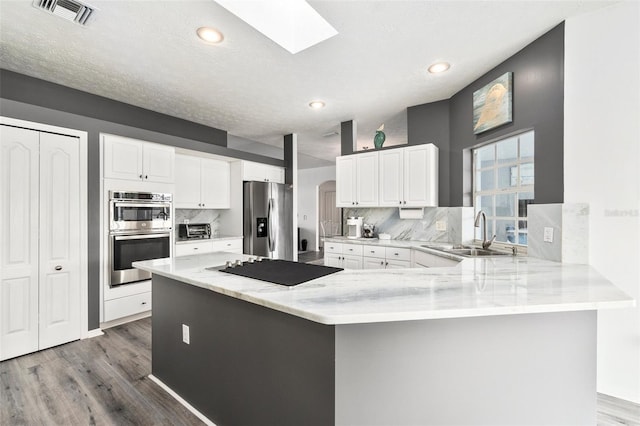 kitchen with decorative backsplash, sink, white cabinetry, a skylight, and appliances with stainless steel finishes