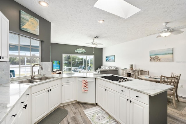 kitchen with a skylight, kitchen peninsula, a textured ceiling, white cabinets, and sink