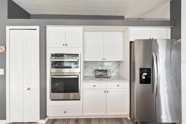 kitchen featuring a textured ceiling, white cabinets, appliances with stainless steel finishes, wood-type flooring, and decorative backsplash