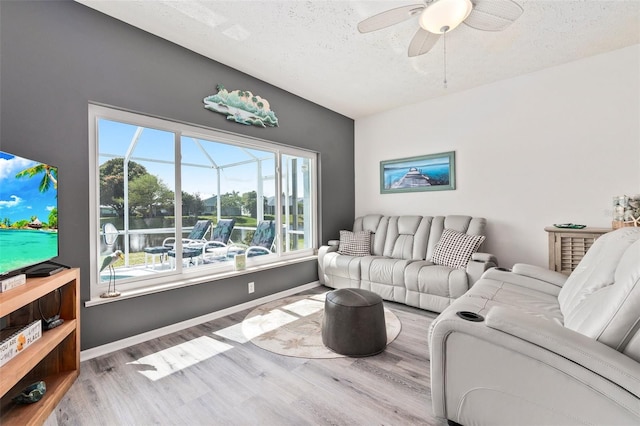 living room with ceiling fan, a textured ceiling, and light wood-type flooring