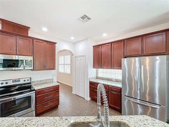 kitchen with appliances with stainless steel finishes, arched walkways, visible vents, and light stone countertops