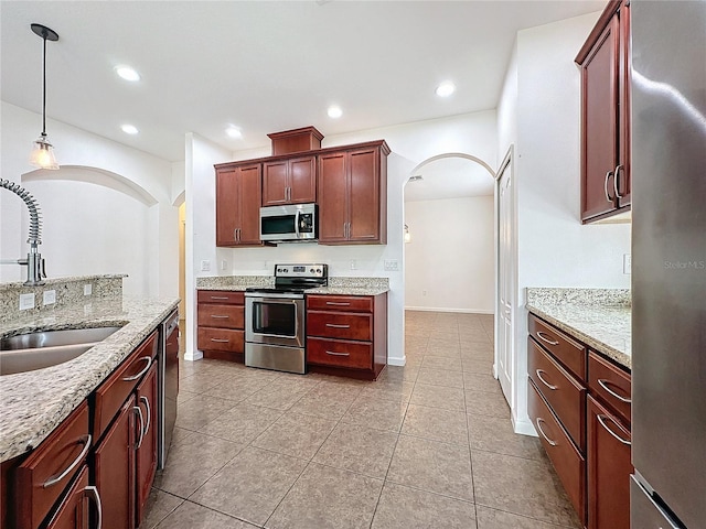 kitchen featuring arched walkways, light stone counters, appliances with stainless steel finishes, pendant lighting, and a sink