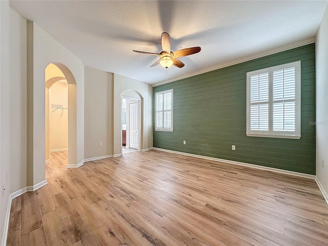 unfurnished room with arched walkways, light wood-style floors, a ceiling fan, a textured ceiling, and baseboards