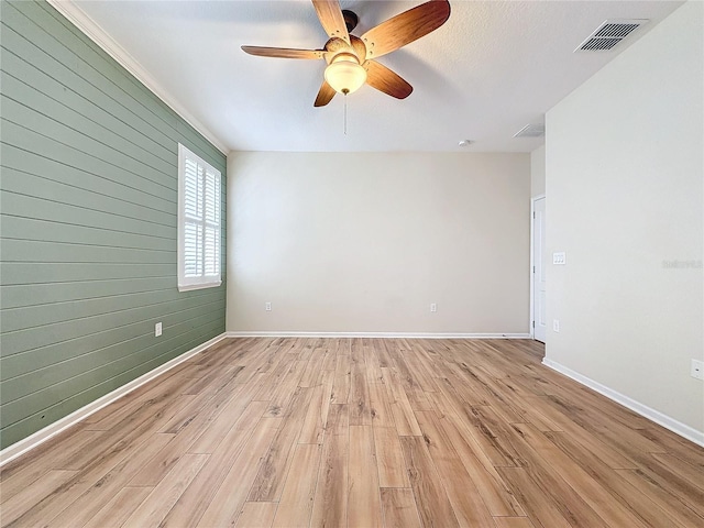 spare room with light wood-style flooring, wood walls, visible vents, and baseboards