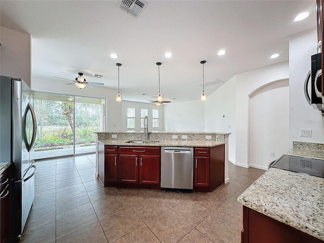 kitchen featuring reddish brown cabinets, a center island with sink, stainless steel appliances, visible vents, and a sink