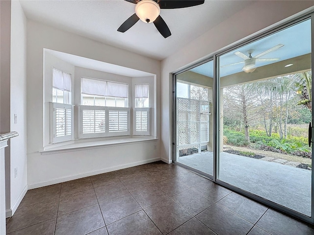 interior space with dark tile patterned floors, a ceiling fan, and baseboards