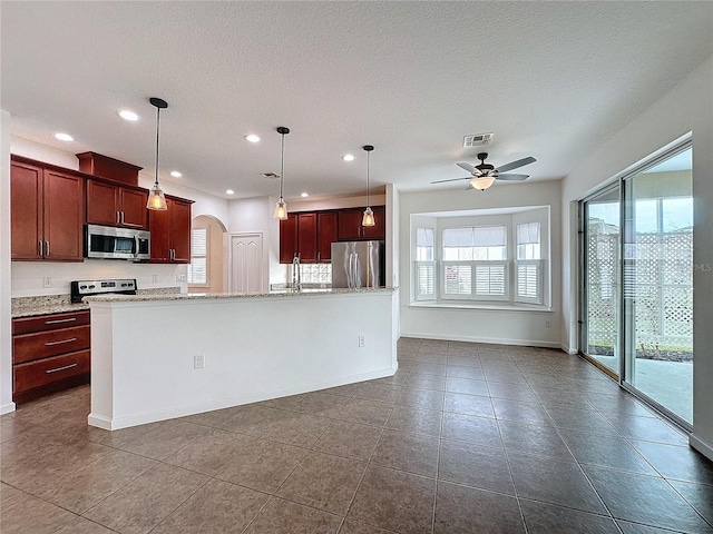 kitchen featuring a center island with sink, visible vents, arched walkways, appliances with stainless steel finishes, and decorative light fixtures