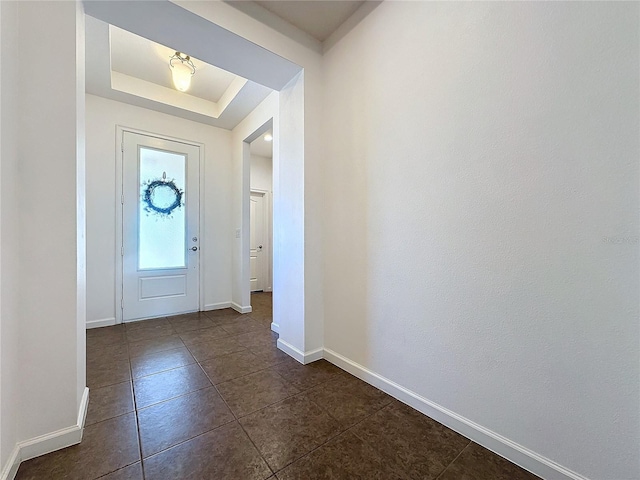 foyer entrance featuring dark tile patterned floors, baseboards, and a tray ceiling