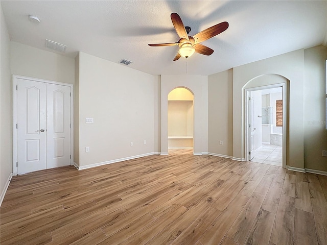 empty room with light wood finished floors, visible vents, arched walkways, baseboards, and ceiling fan