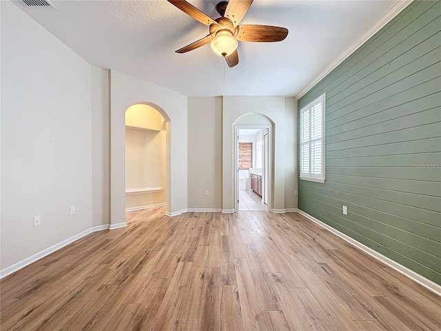 empty room with a textured ceiling, baseboards, light wood-style flooring, and wooden walls