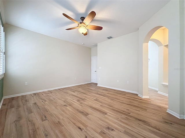 empty room featuring arched walkways, ceiling fan, light wood-style flooring, and visible vents