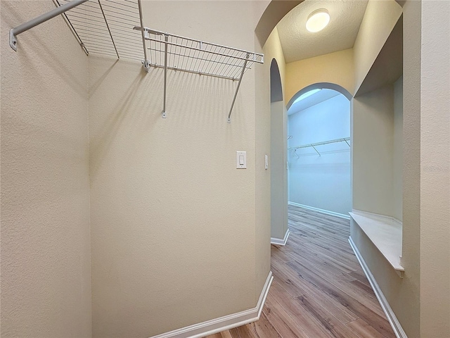 walk in closet featuring light wood-style floors and arched walkways