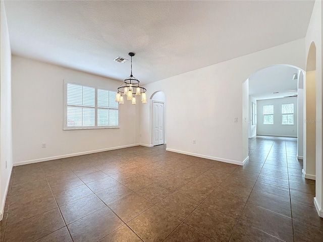 unfurnished room featuring arched walkways, a notable chandelier, dark tile patterned flooring, visible vents, and baseboards