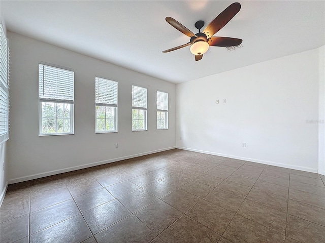 empty room featuring dark tile patterned floors, plenty of natural light, visible vents, and baseboards