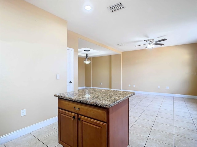 kitchen with light tile patterned floors, ceiling fan, decorative light fixtures, stone countertops, and a kitchen island