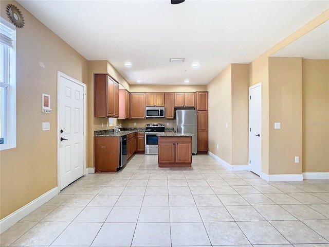 kitchen with light tile patterned flooring, stainless steel appliances, light stone counters, and a center island