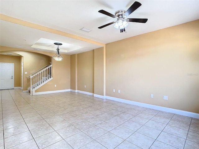 tiled empty room with ceiling fan and a tray ceiling