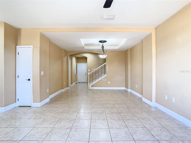 unfurnished room with a raised ceiling, light tile patterned floors, and ceiling fan