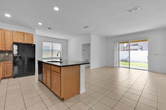 kitchen featuring sink, a center island with sink, light tile patterned floors, and black appliances