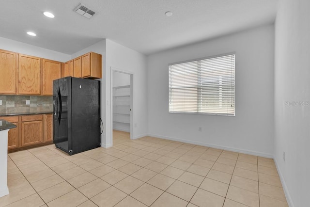 kitchen featuring tasteful backsplash, light tile patterned flooring, and black fridge