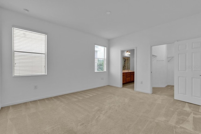 unfurnished bedroom with a walk in closet, light colored carpet, ensuite bath, and a closet