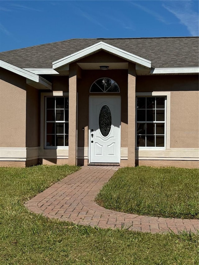 property entrance with roof with shingles, a lawn, and stucco siding