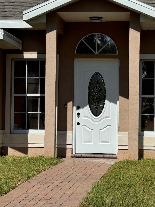 entrance to property featuring a shingled roof and stucco siding