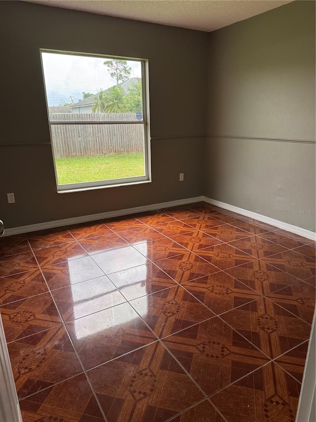 spare room with a textured ceiling, dark tile patterned flooring, and baseboards