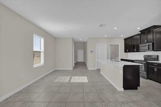 kitchen with light tile patterned floors, a center island with sink, a breakfast bar area, appliances with stainless steel finishes, and sink