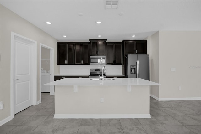 kitchen featuring light tile patterned floors, appliances with stainless steel finishes, a center island with sink, and sink