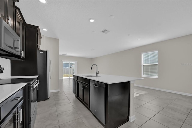 kitchen with sink, a kitchen island with sink, stainless steel appliances, a textured ceiling, and light tile patterned floors